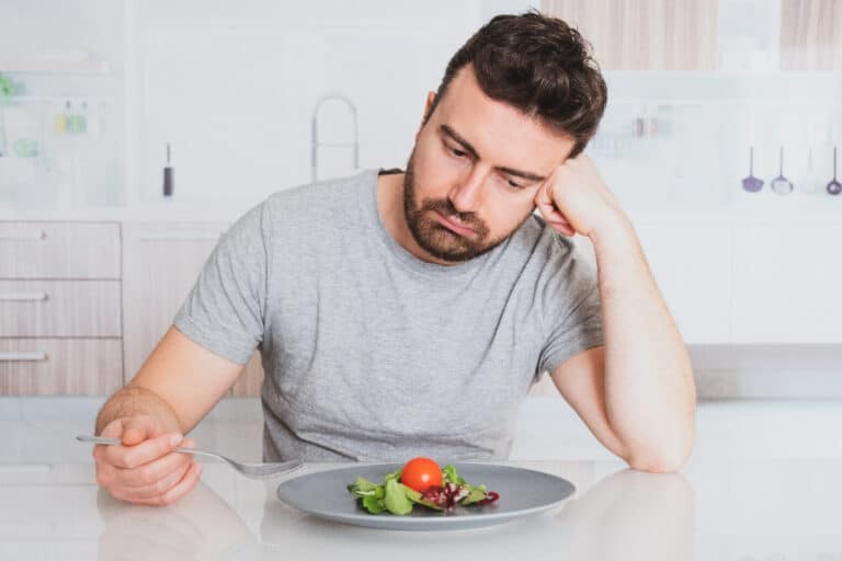 Man sits at a table looking at a small plate of salad looking hesitant to eat.